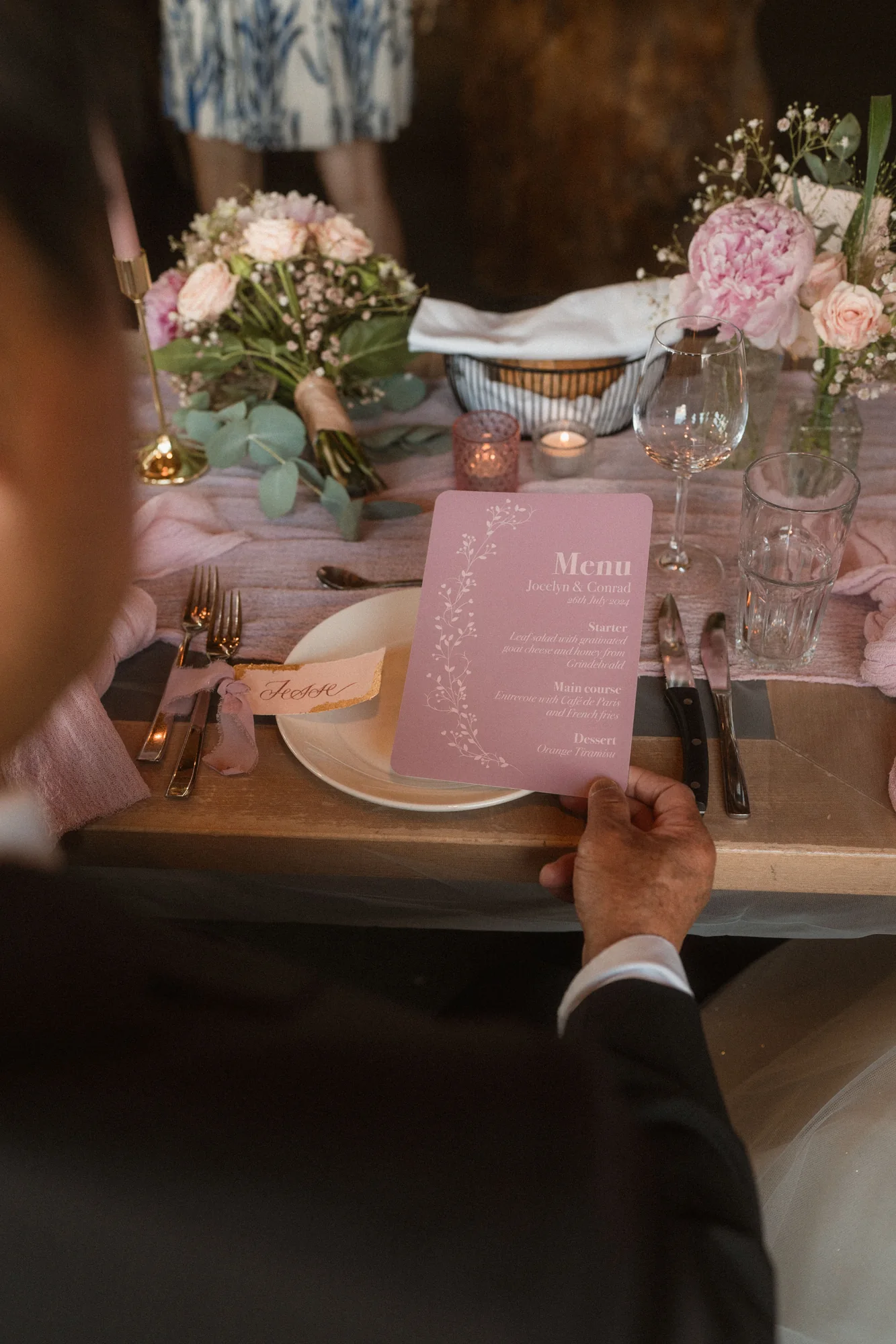 Gast mit roséfarbenem Hochzeitsmenü an einem blumengeschmückten Gedeck