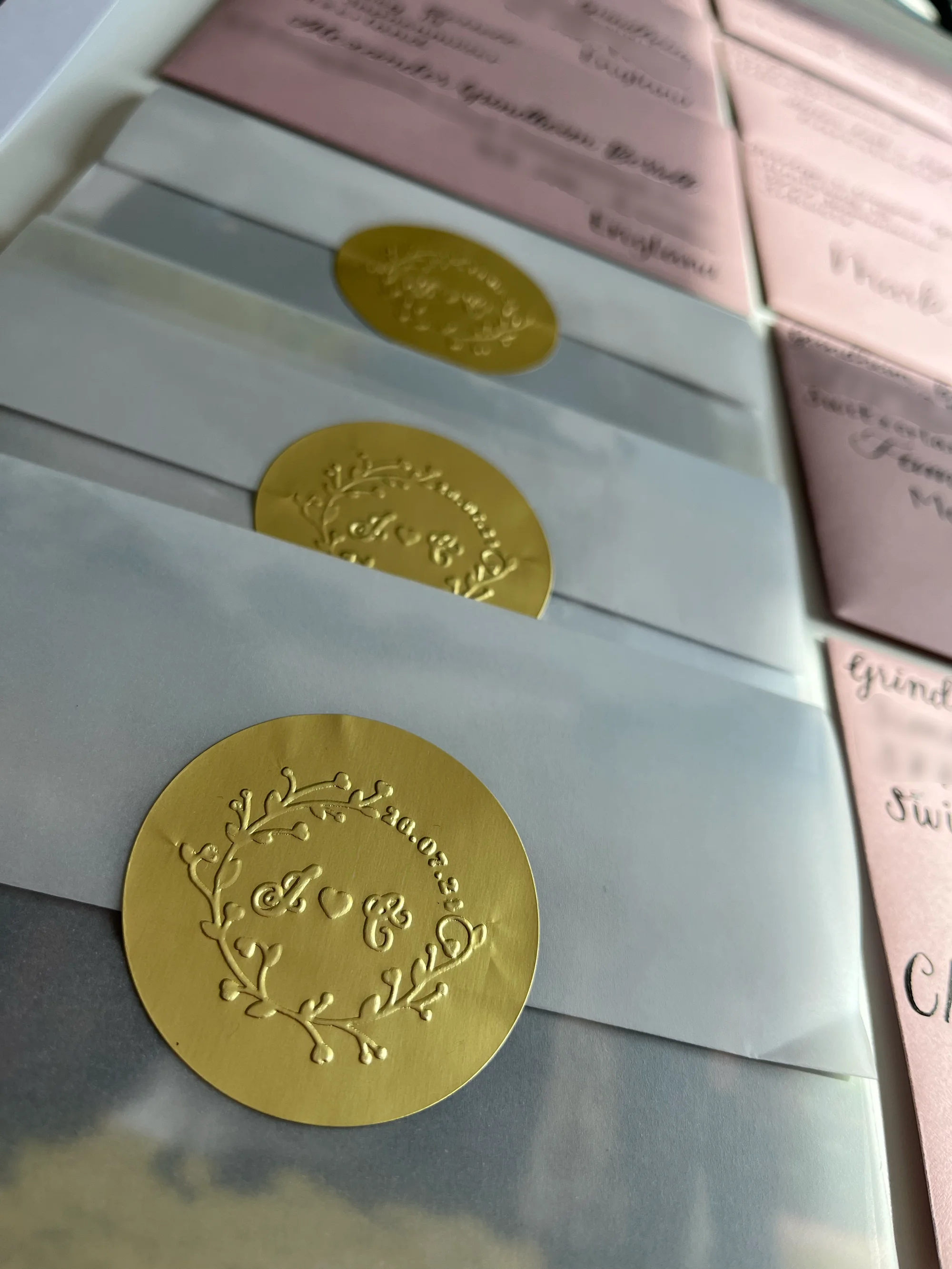 Weisse Couverts mit goldenen Signet-Siegeln neben handbeschrifteten roséfarbenen Couverts