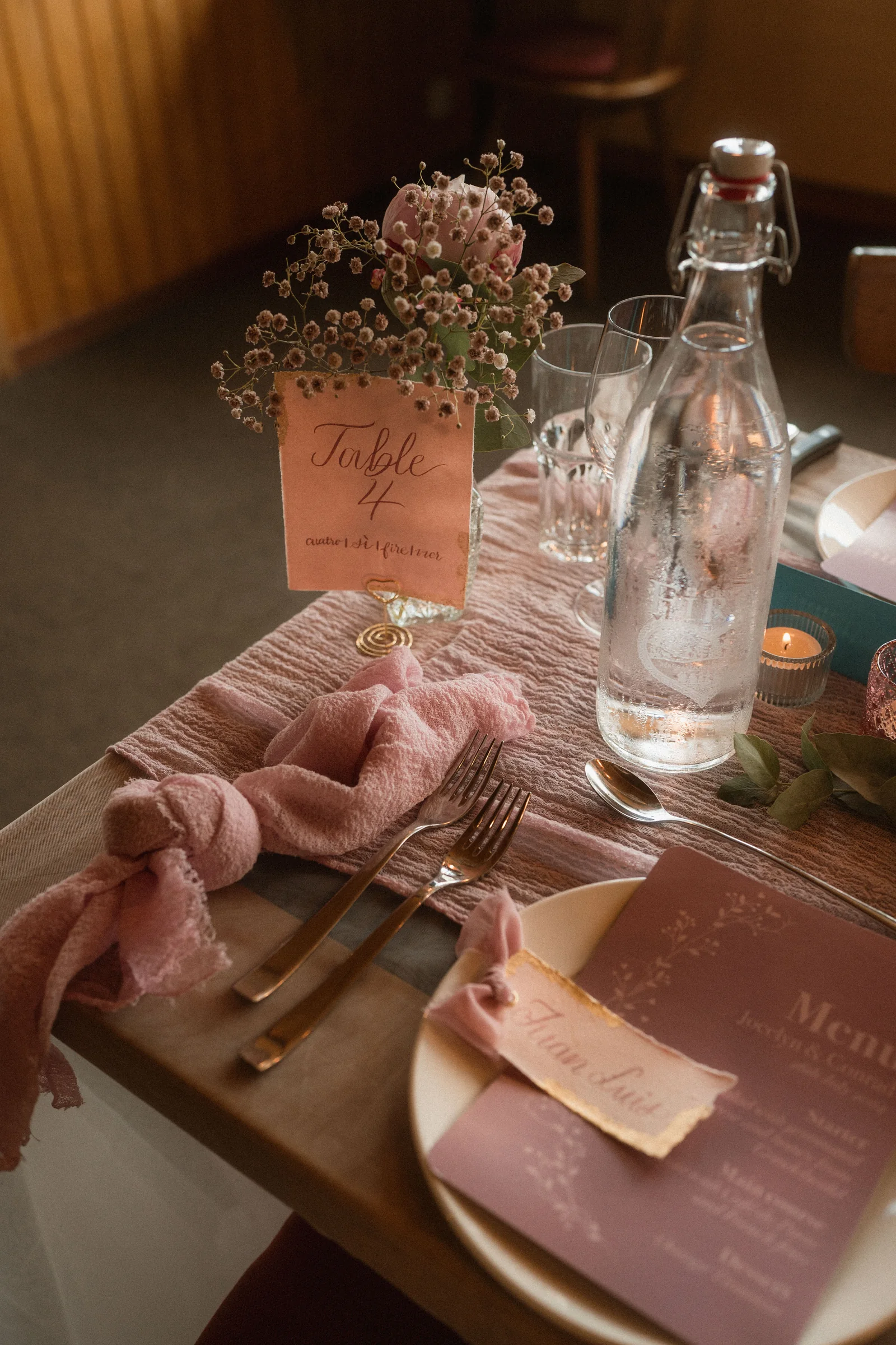 Handbeschriftete Tischkarte zwischen roséfarbenen Blumen und Hochzeitsgedeck