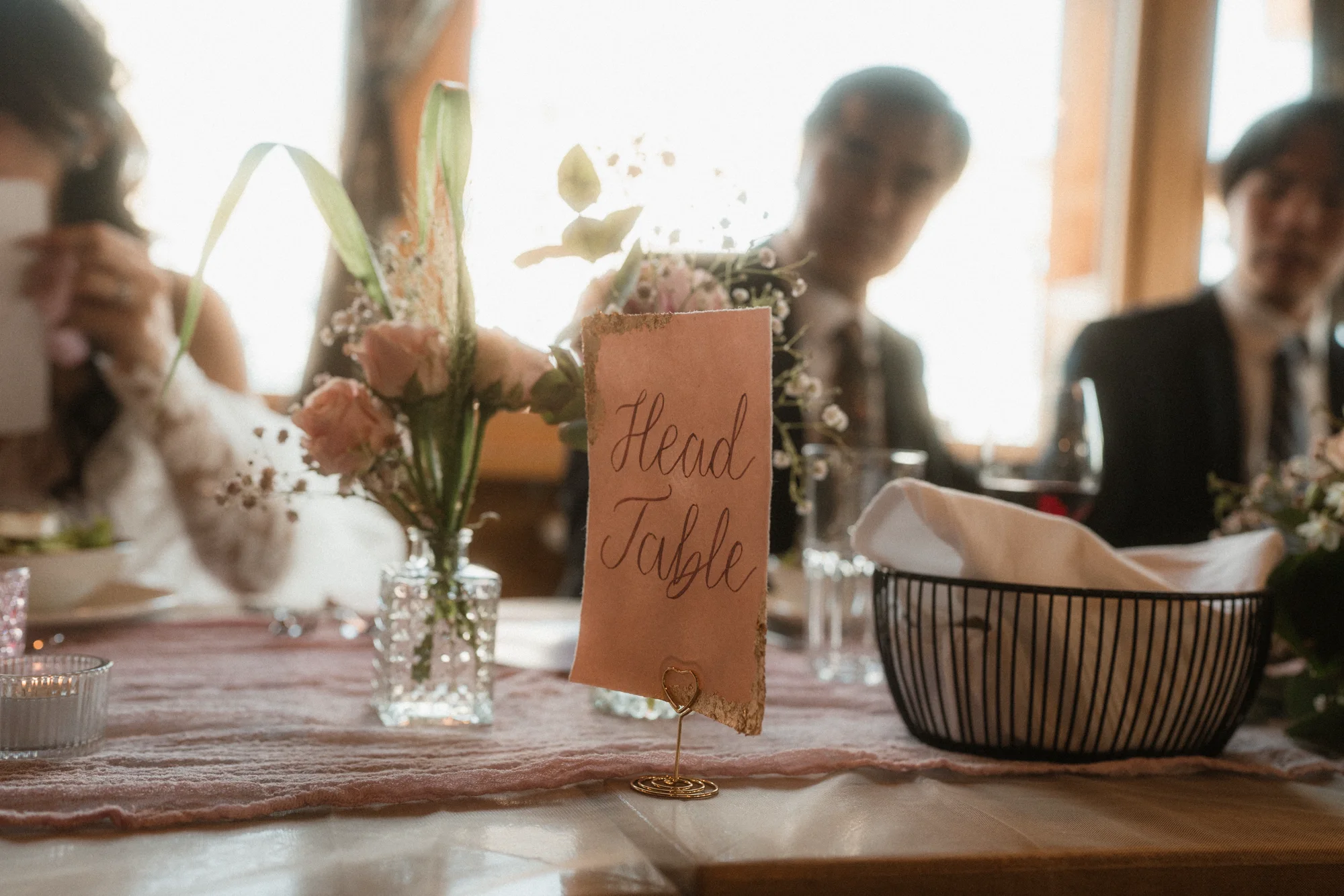 Handbeschriftete Karte für den Brauttisch zwischen roséfarbenen Hochzeitsblumen