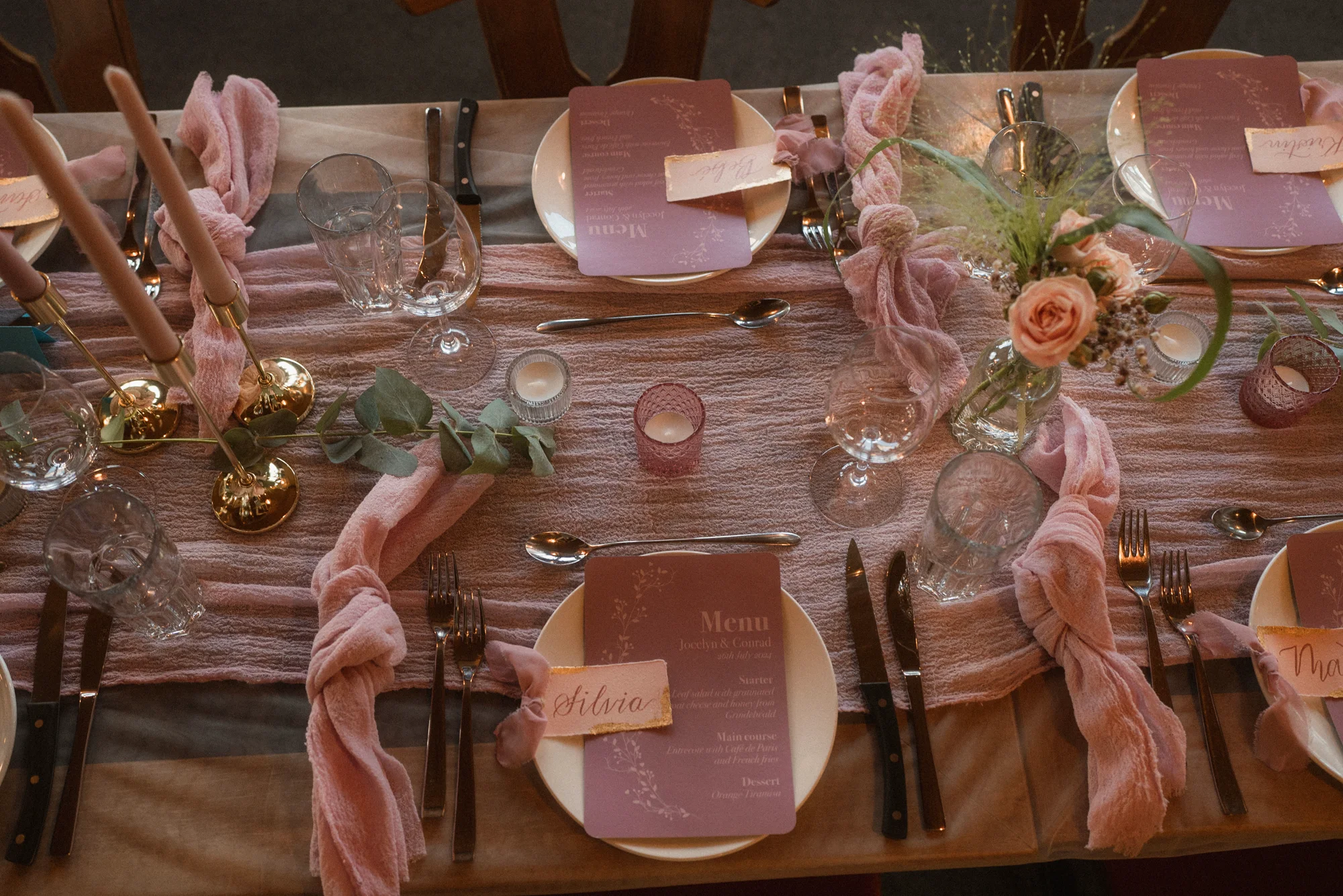 Roséfarbener Hochzeitstisch mit handbeschrifteten Menüs und Platzkarten